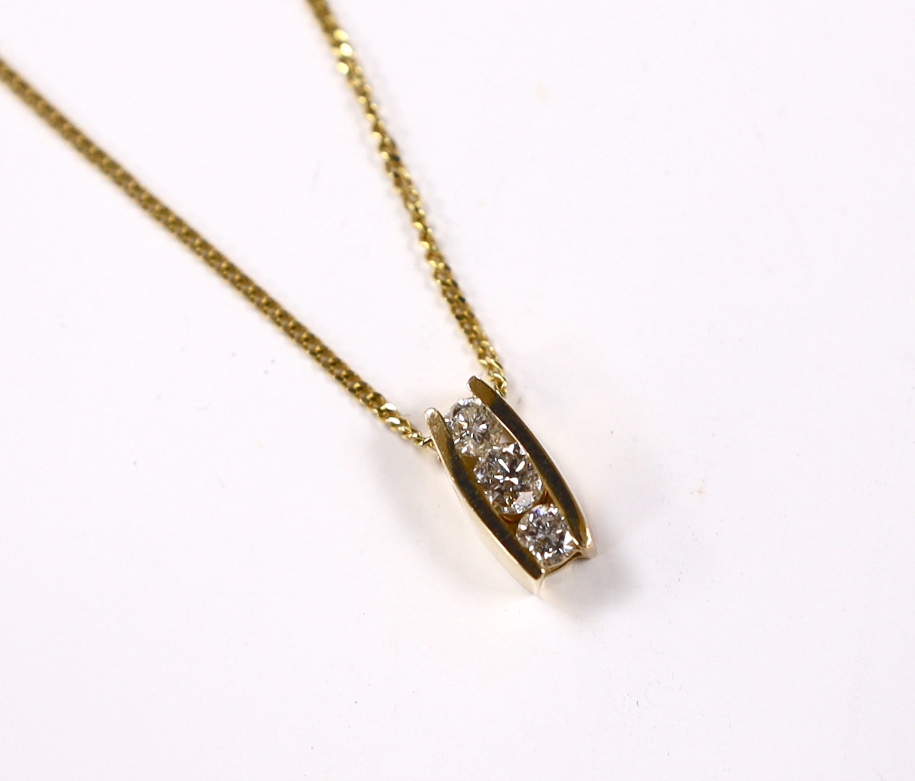 A modern yellow metal and three stone diamond set pendant, 10mm, on a modern 9ct gold fine link chain, 44cm, gross weight 3.1 grams.